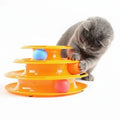 Cat playing with a three-tiered orange cat toy with colorful balls on a white background